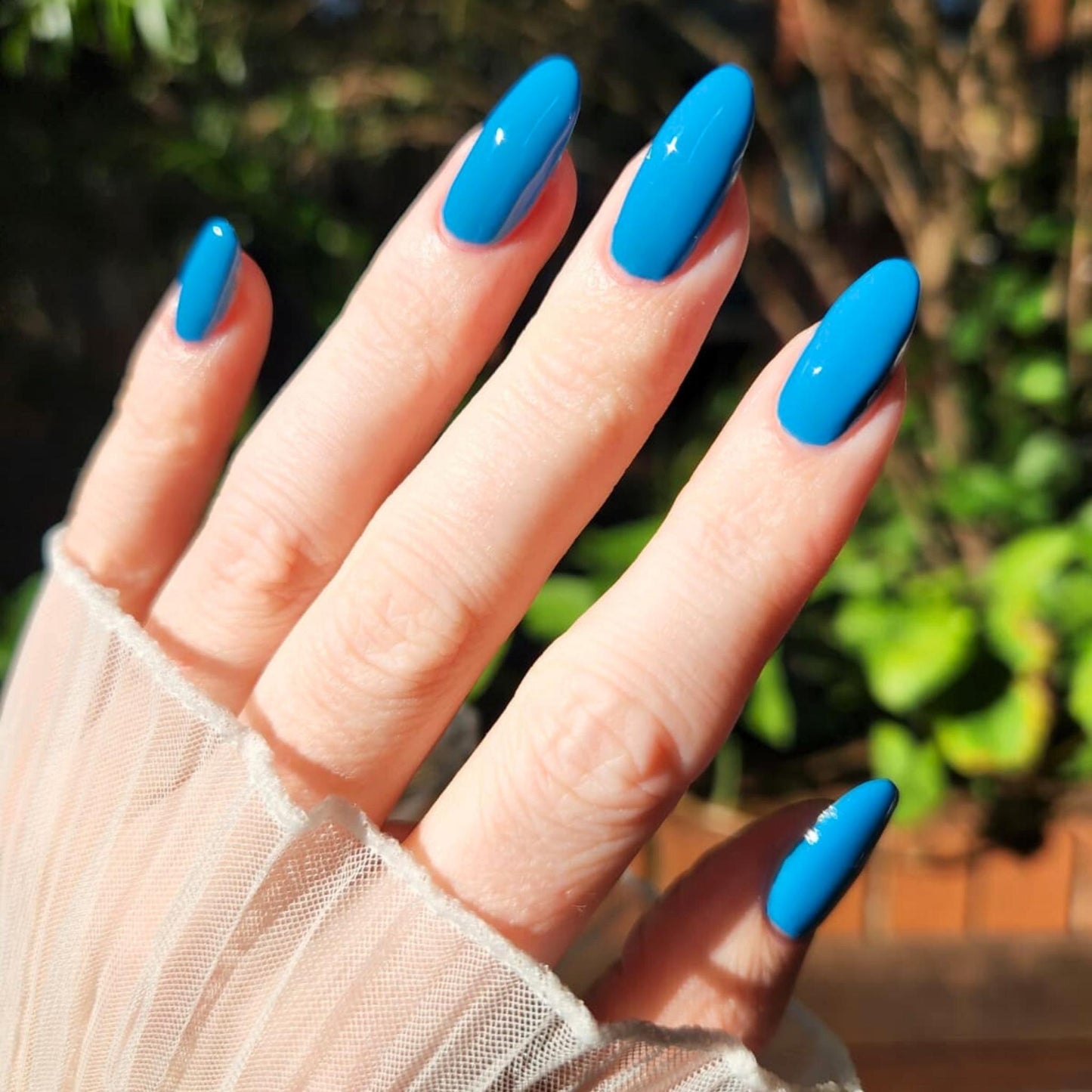 Hand with bright blue nail polish against a blurred green background