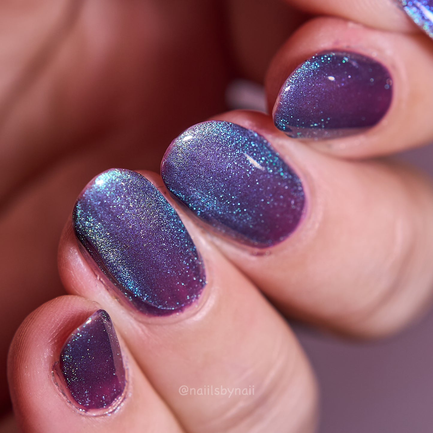 Close-up of a hand with purple and green magnetic nail polish in velvet cat eye effect