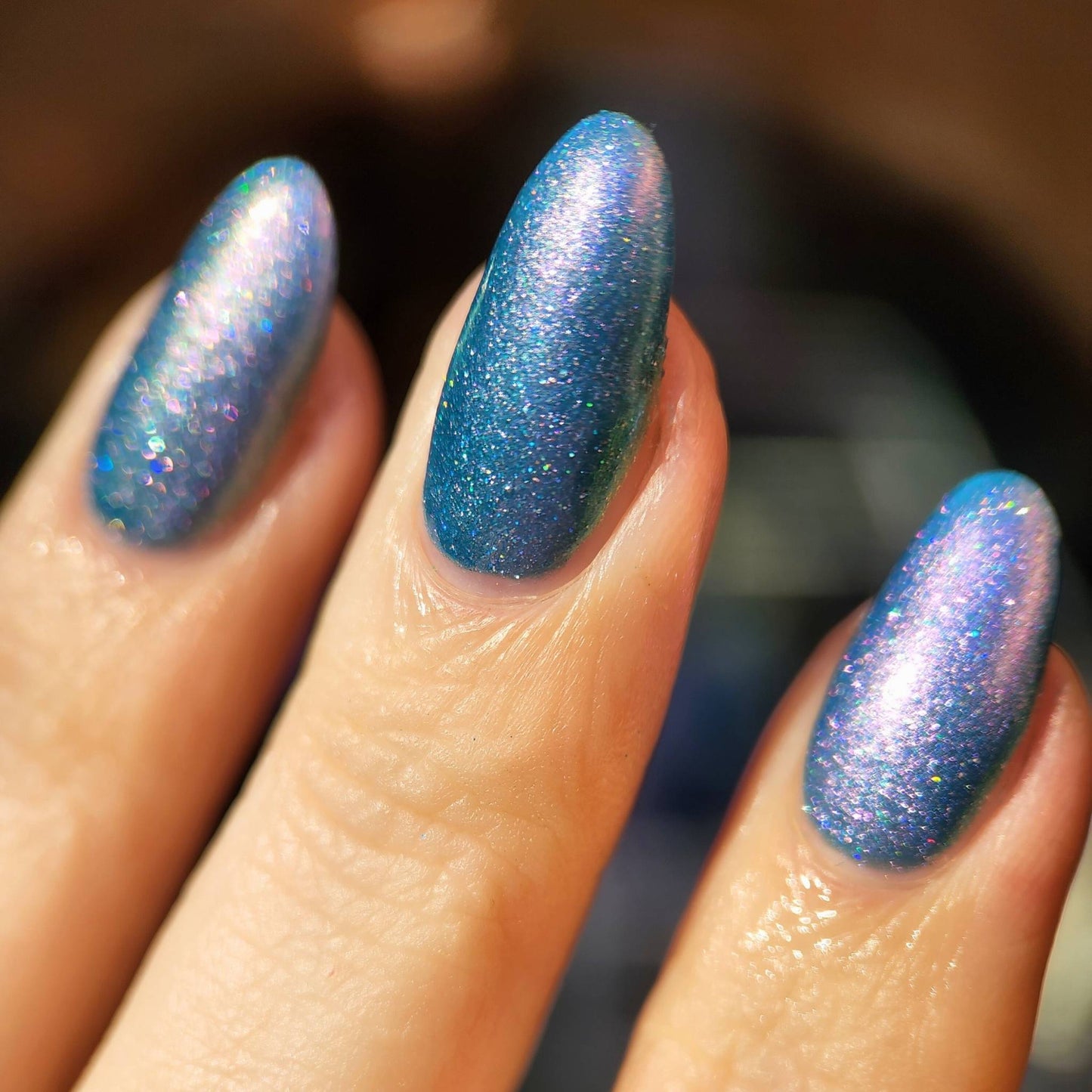 Close-up of a hand with blue glittery nail polish on a blurred background