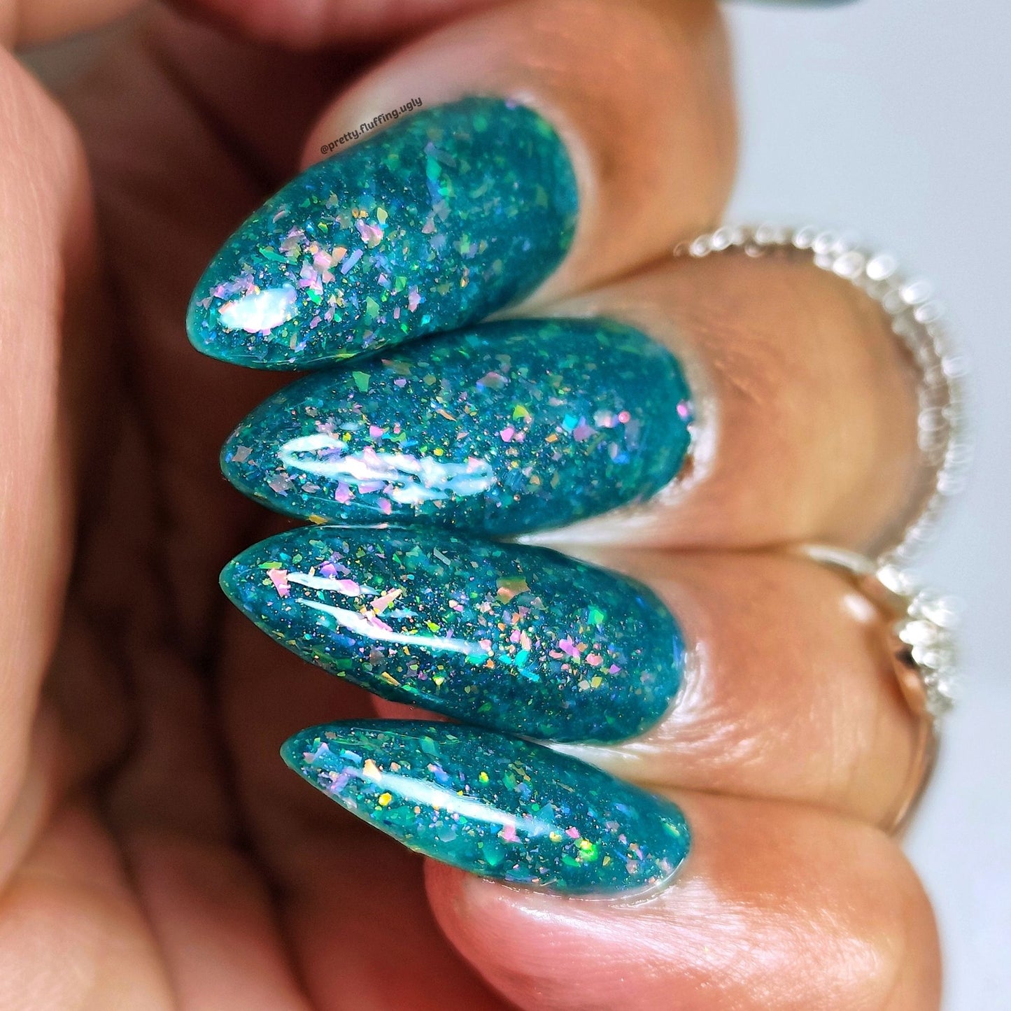 Swatch of teal jelly polish with gold-to-pink shimmer on dark skin tone