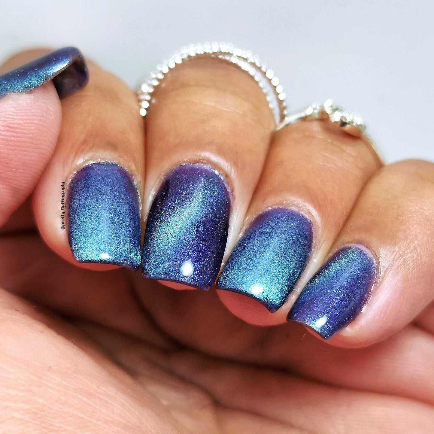 Close-up of a hand with blue and purple gradient nail polish on a neutral background