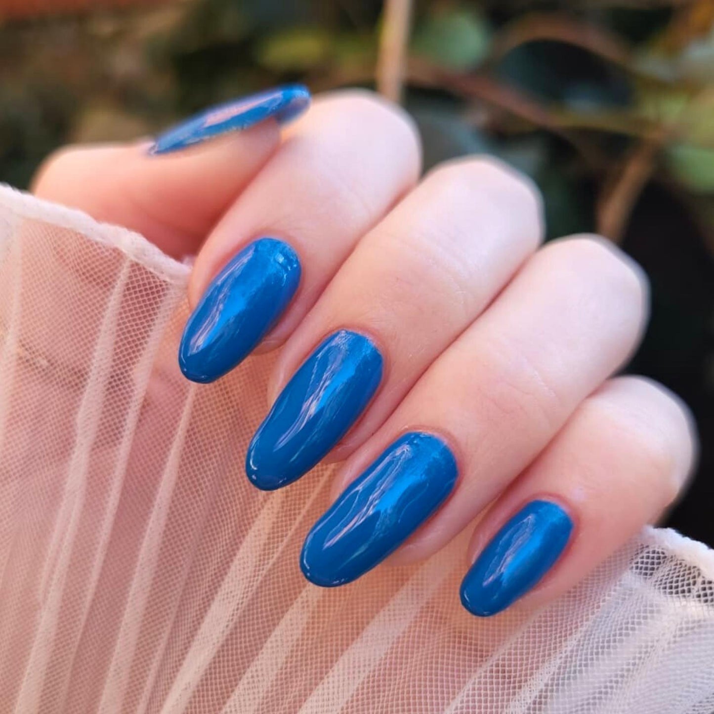 Hand with blue nail polish on a blurred natural background