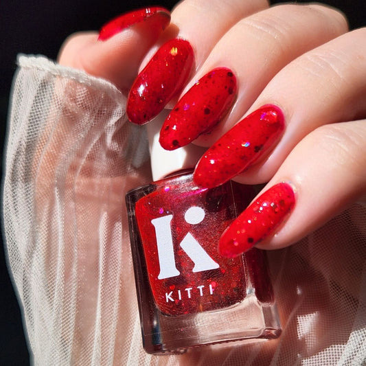 Hand with red glittery christmas nail polish holding a bottle of KITTI nail polish.