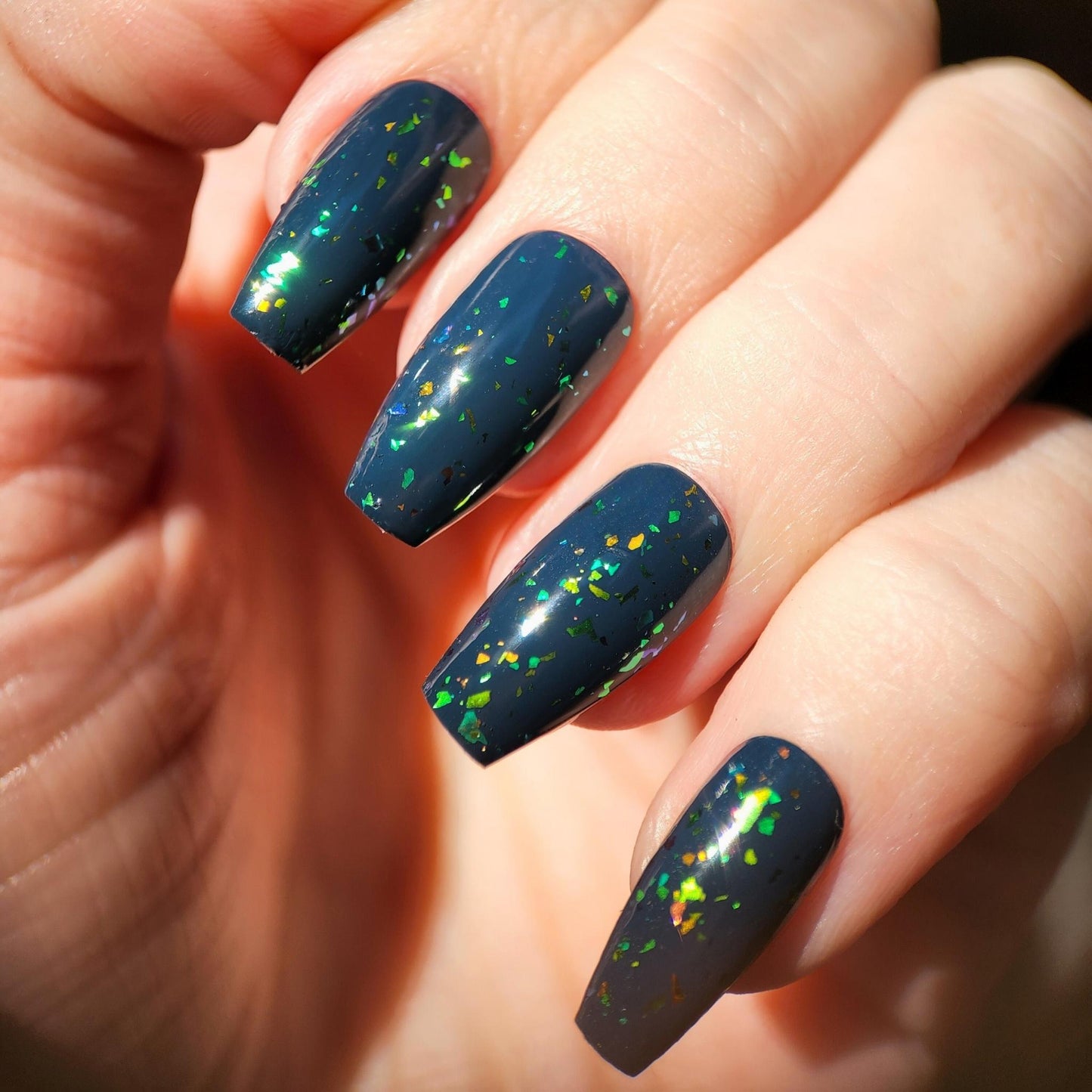 Vegan flakie topper over dark base polish with dramatic shimmer