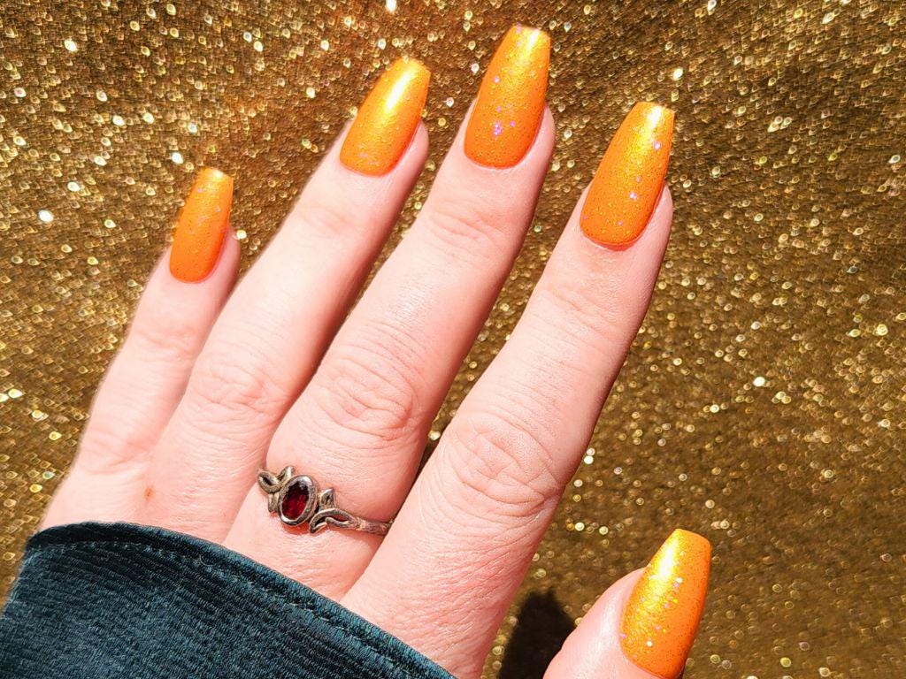 Long-lasting orange nail polish with holo glitter – swatched on fair skin