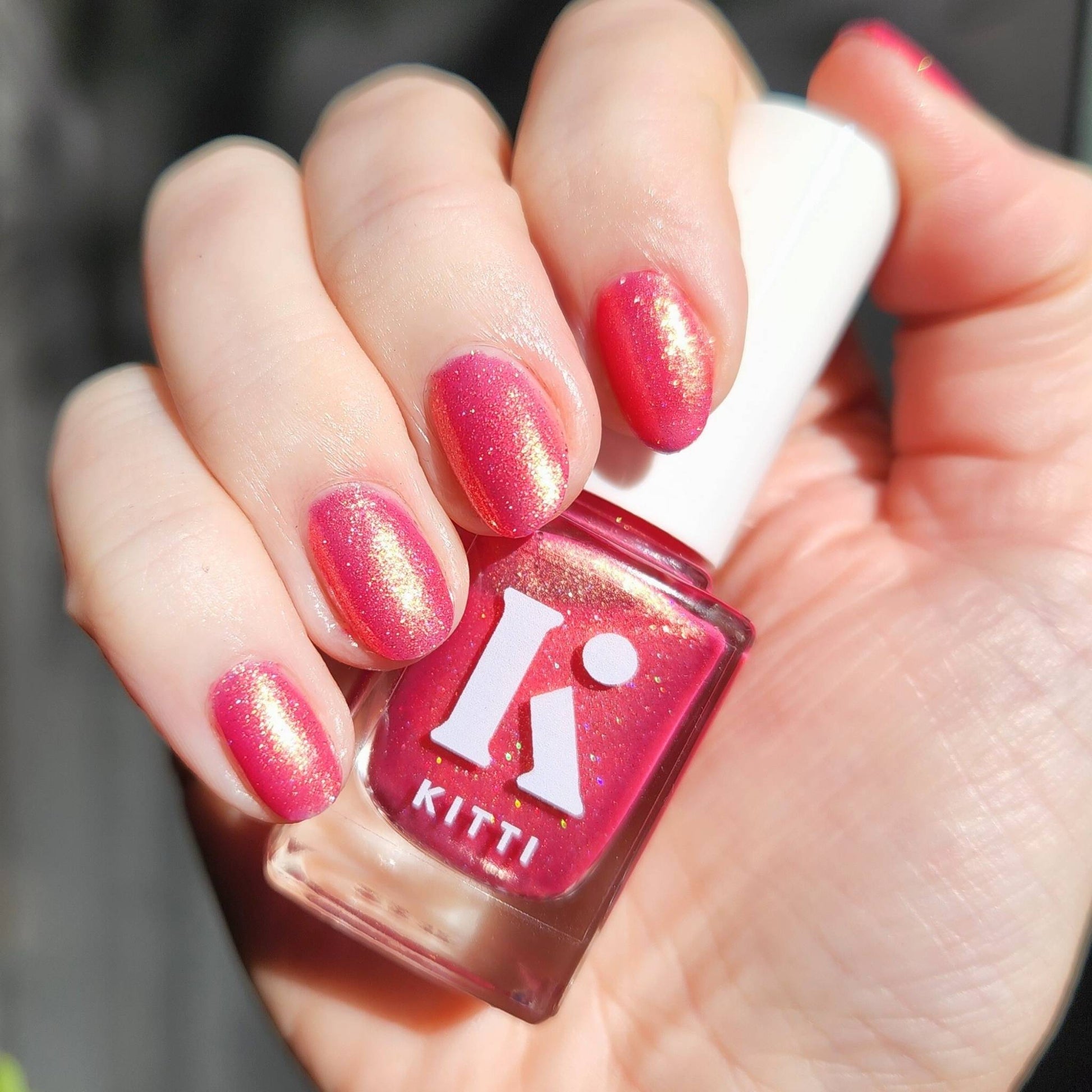 Hand with pink glittery nails holding a bottle of Kitti nail polish.