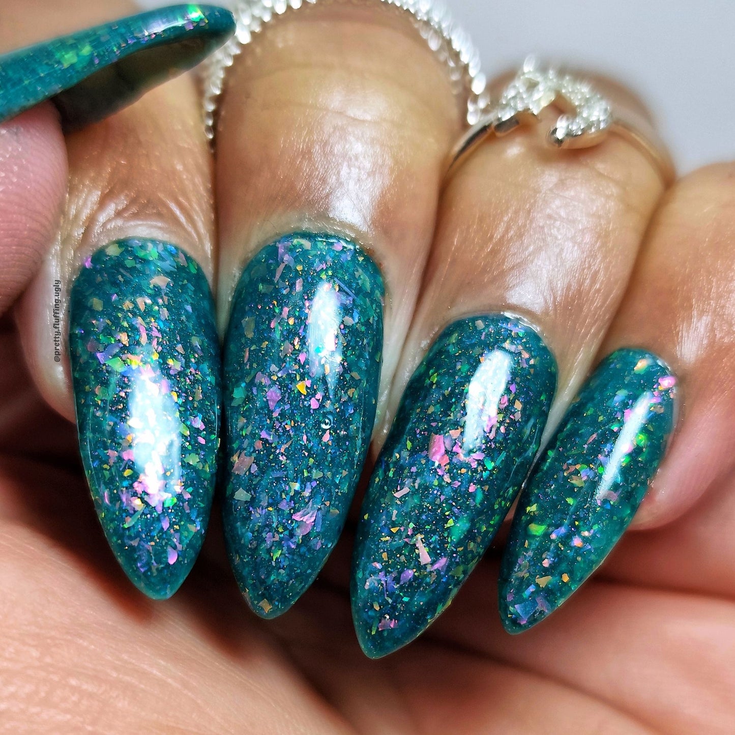 Teal jelly nail polish with sparkly iridescent flakes on dark skin tone