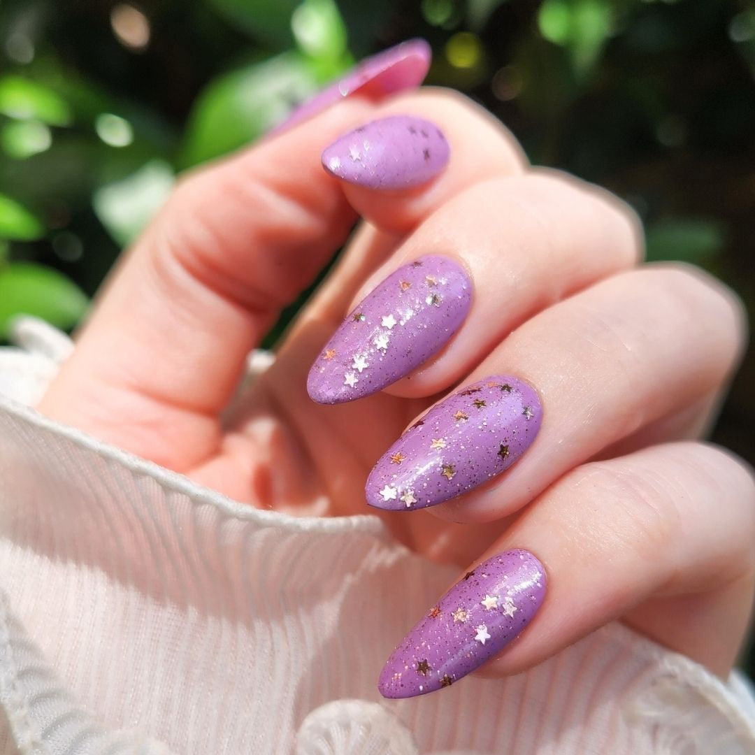 Champagne Popper nail polish topper bottle next to purple glitter manicure outdoors in natural light