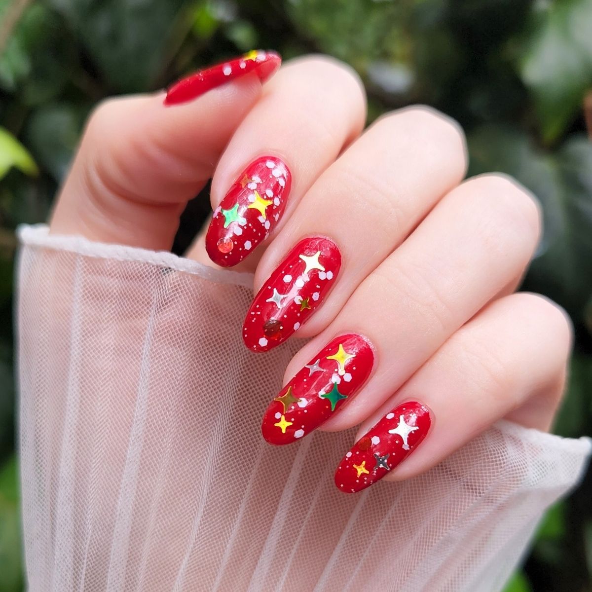 Hand with christmas nail polish featuring Christmas-themed decorations against a green leafy background