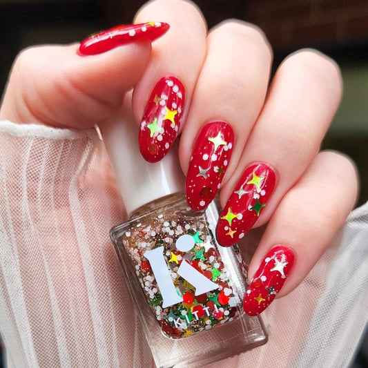 Hand with red nail polish featuring Christmas designs holding a nail polish bottle with festive design.