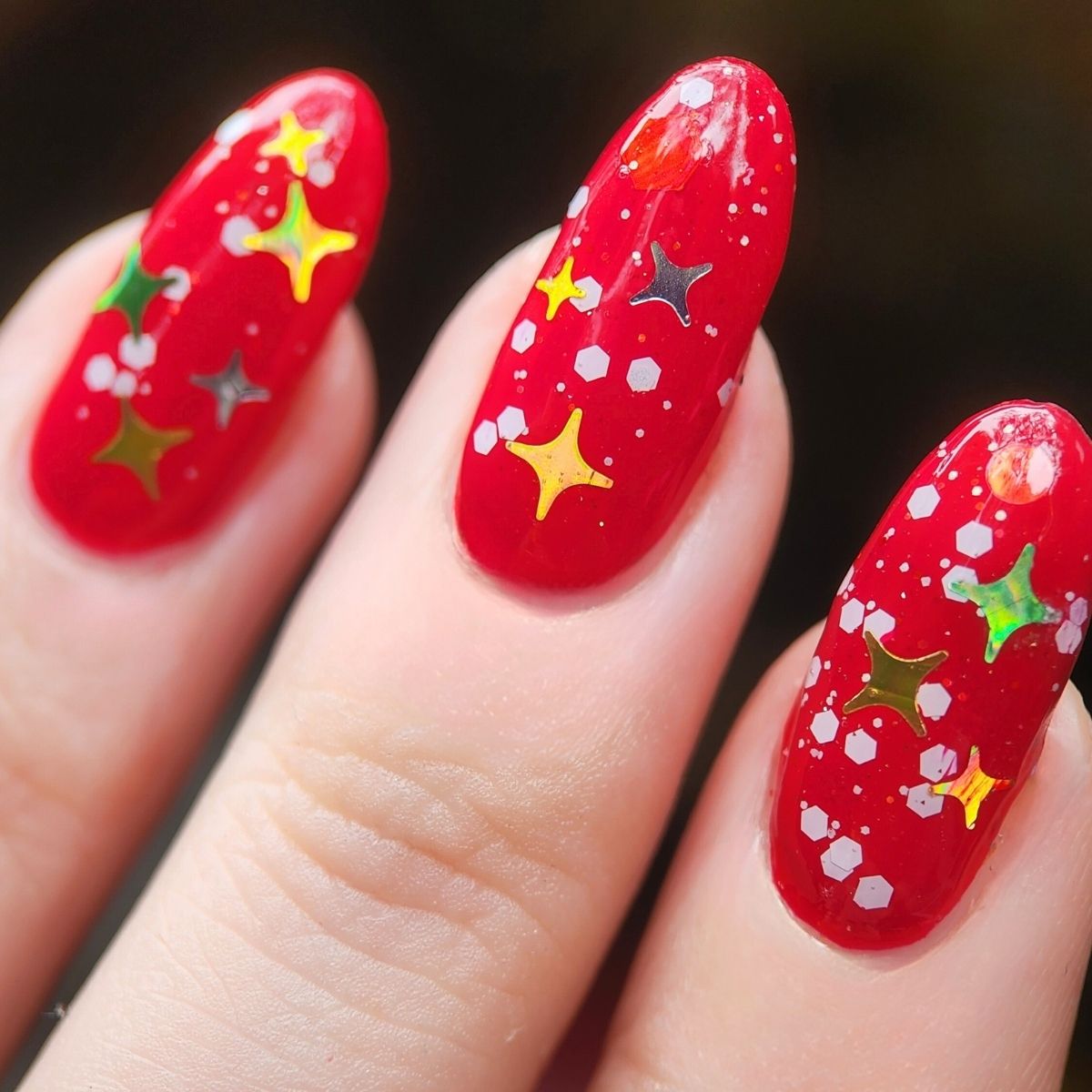 Red nail polish with Christmas star designs on a hand with light skin