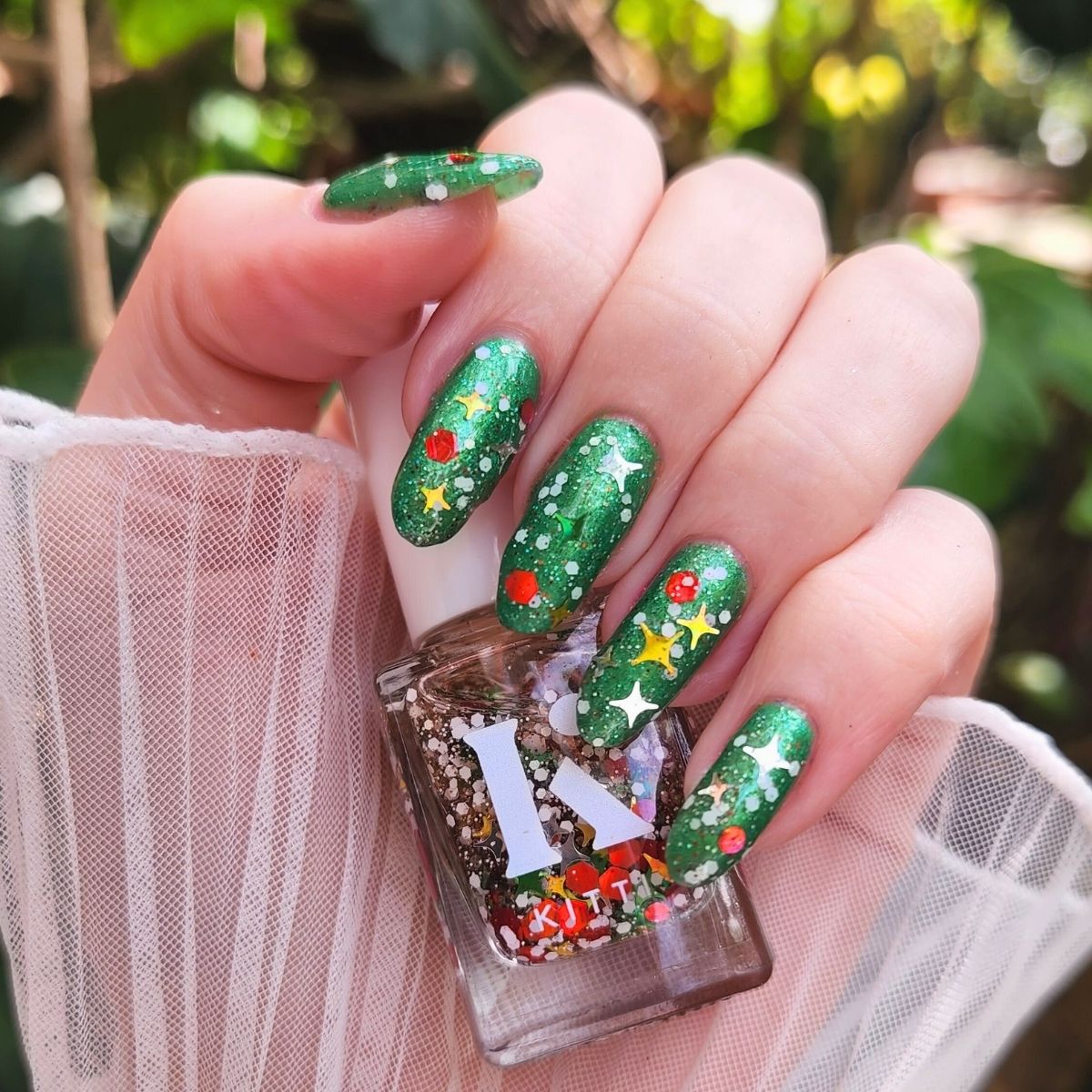 Close-up of Santa’s Afterparty — a holographic christmas nail polish topper with holographic stars and snowy white glitter, shown layered over green nails