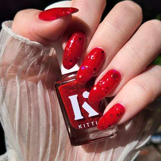 Hand with red glittery nails holding a bottle of KITTI nail polish.