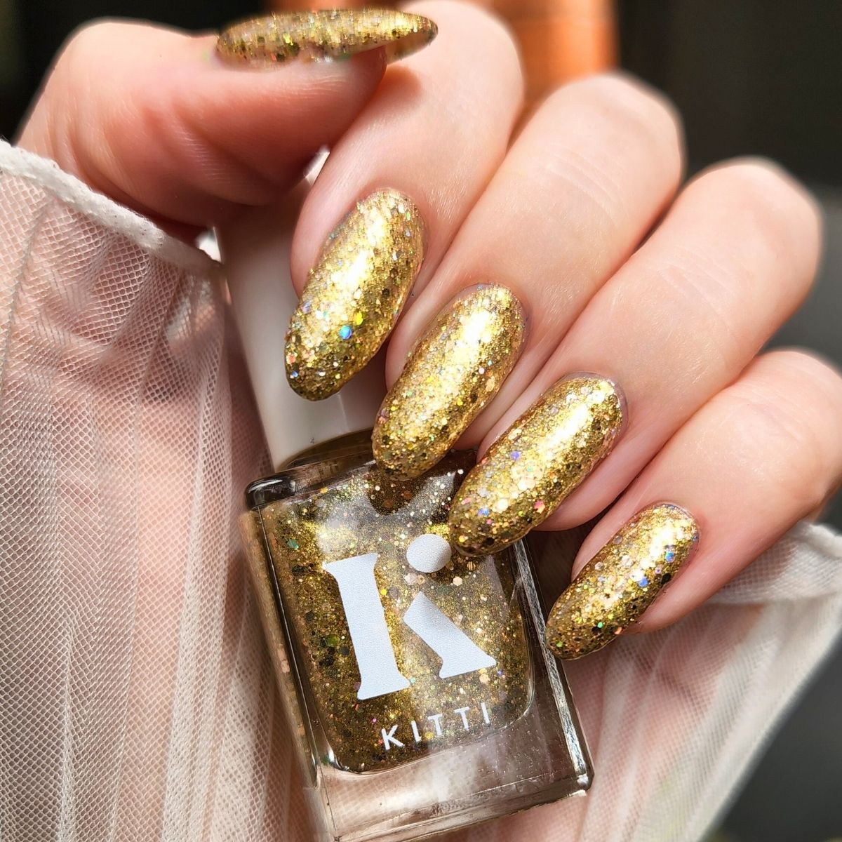 Gold glitter nail polish bottle with matching nails held by a hand