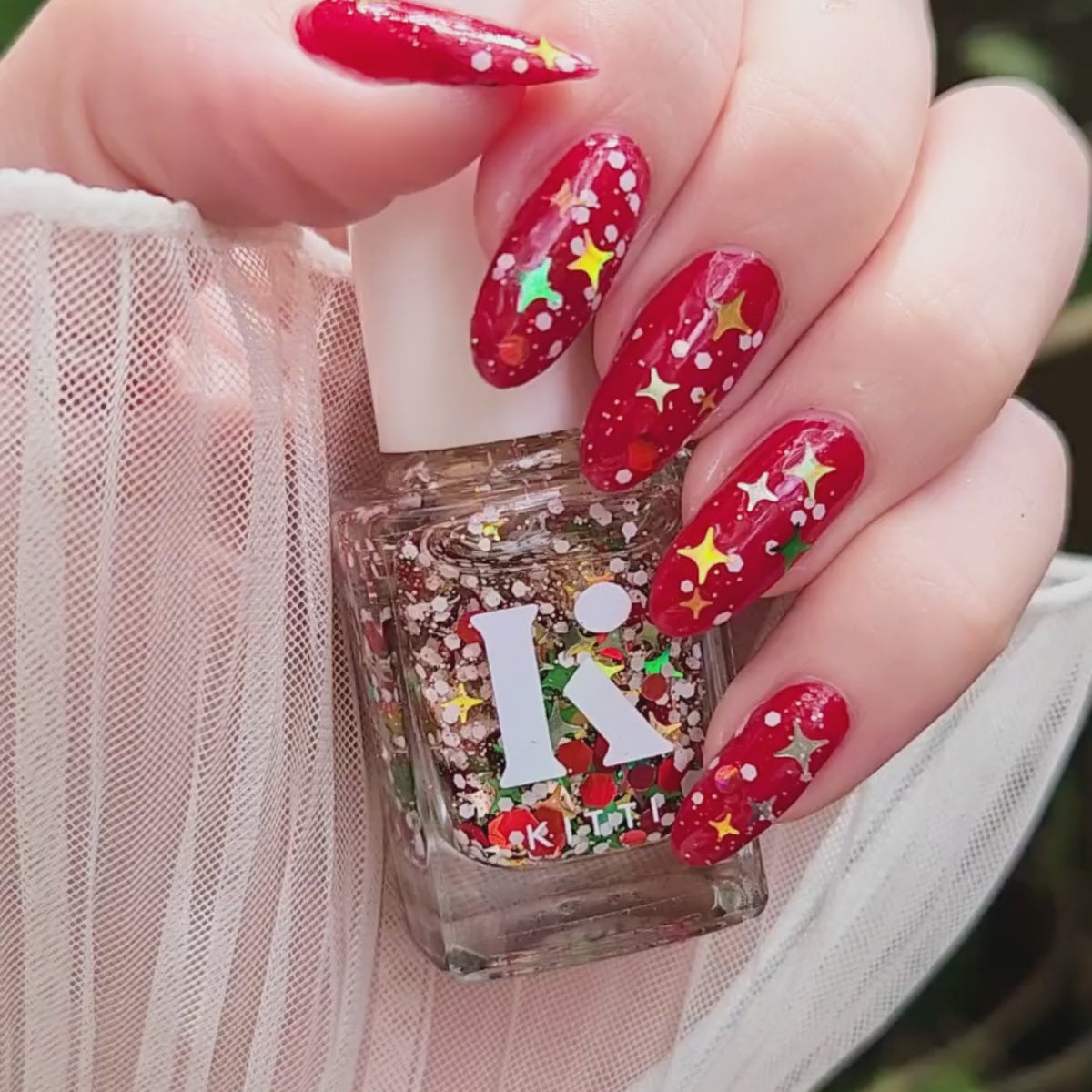 Close-up video of Santa’s Afterparty — a holographic festive nail polish topper with holo stars and snowy white glitter, shown layered over red nails.