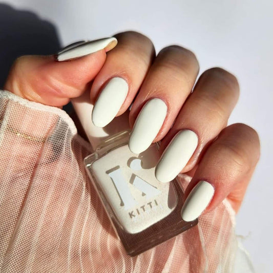 Hand with white nail polish holding a bottle of KITTI nail polish.